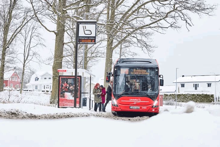 JLT-buss vid en hållplats med snö runtomkring. Tre personer håller på att stiga på bussen. 