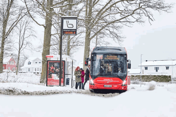 JLT-buss vid en hållplats med snö runtomkring. Tre personer håller på att stiga på bussen.
