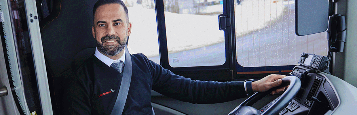 En busschaufför sitter vid förarsätet och tittar på en resenär.