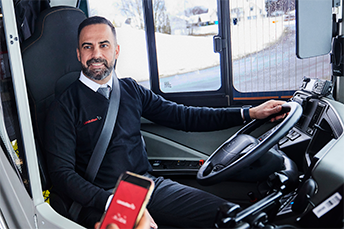 En busschaufför sitter vid förarsätet och tittar på en resenär.