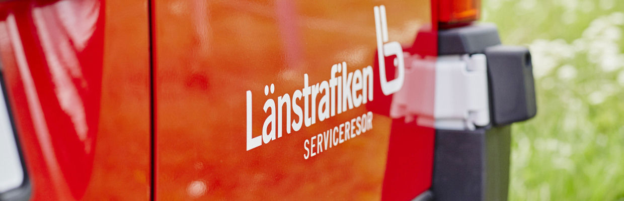 Närbild på en JLT-logotyp som sitter på en röd serviceresebuss.