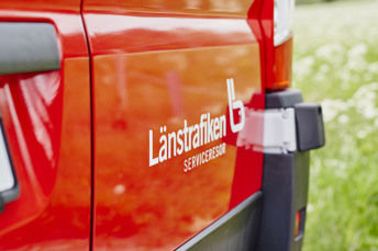 Närbild på en JLT-logotyp som sitter på en röd serviceresebuss.